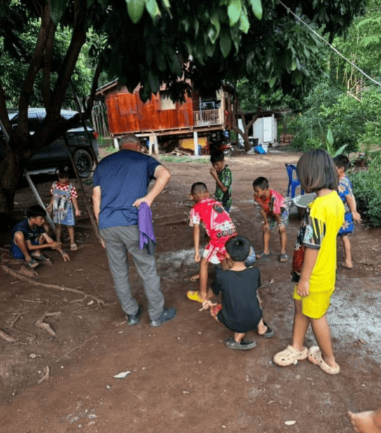 Children and an adult participate in an outdoor community activity in a rural setting.