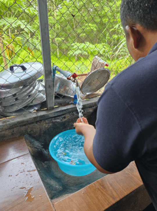 Person washing hands at a clean-water station with a blue basin and running tap.