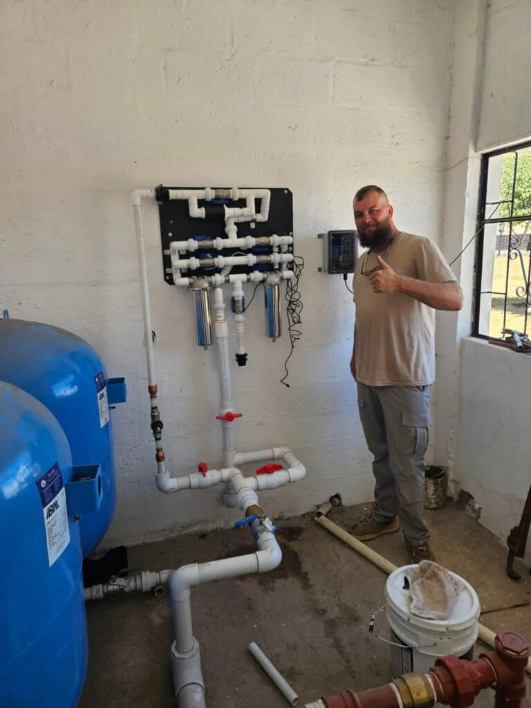 Volunteer standing beside a clean water filtration system during a community outreach project.