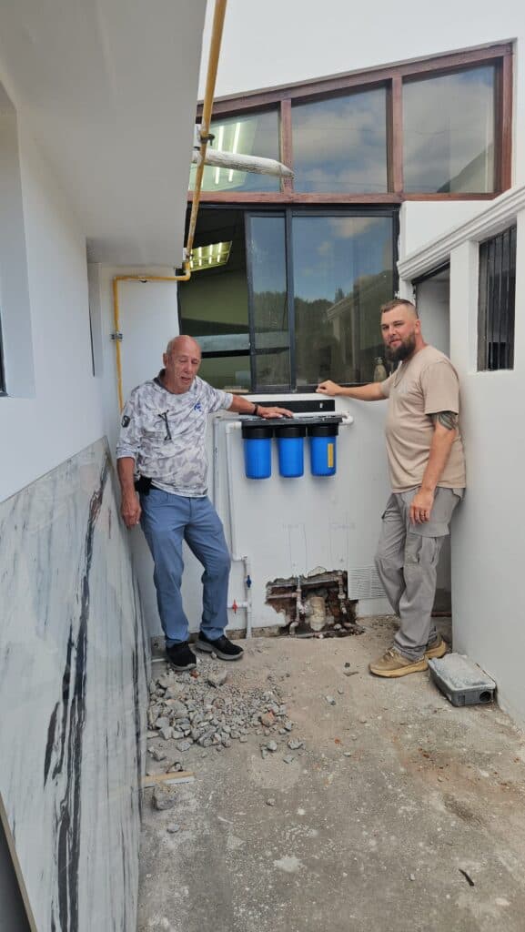 Project partners stand beside a multi-stage water filtration system installed to provide clean water in Ecuador.