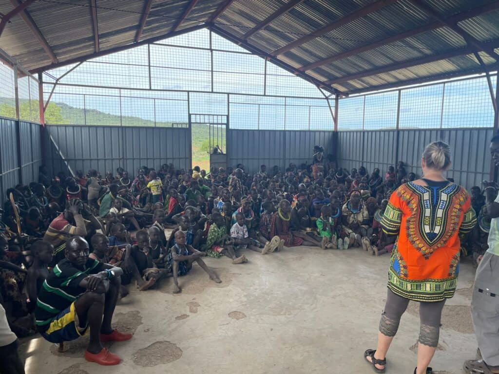 Community outreach gathering in Kenya with local residents seated inside a covered shelter